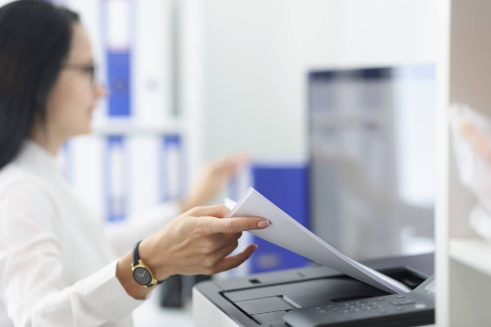 Young woman pulling paper out of printer