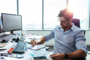 Young Man Making Business Plans With Papers and Computers on His Desk.