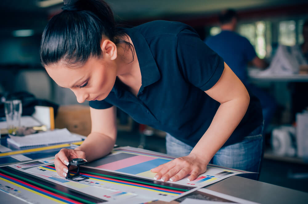 Worker in a Printing and Press Centar Uses a Magnifying Glass and Check the Print Quality