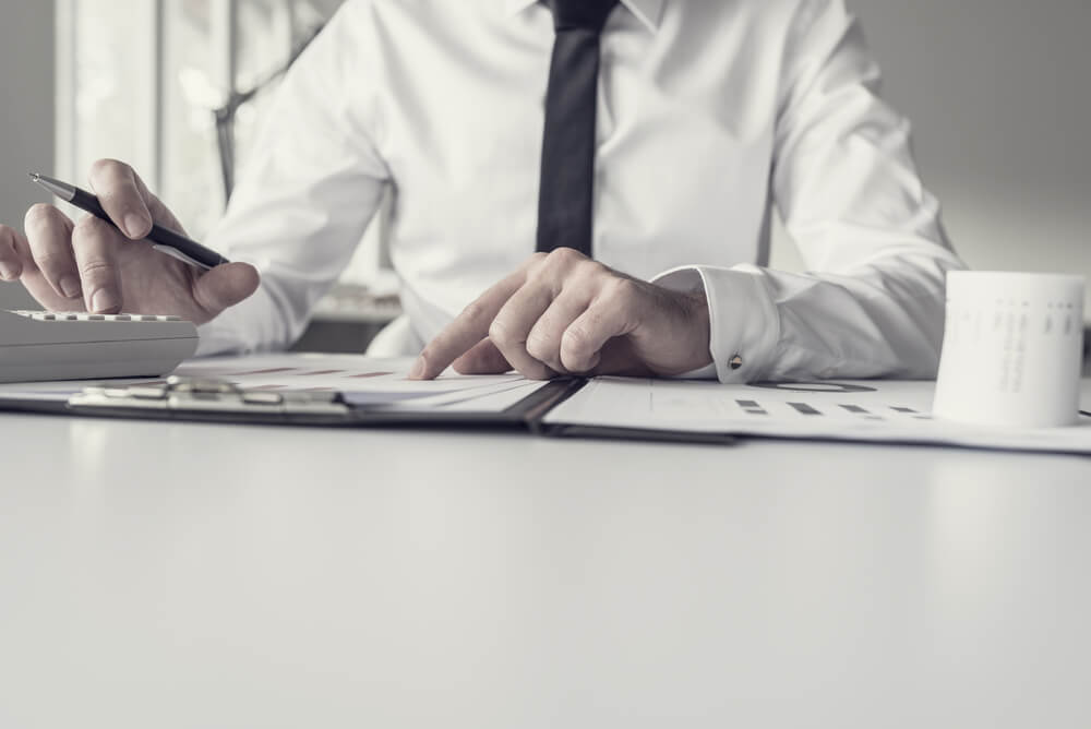 Retro Toned Image of Business Person Checking Facts on Various Printed Paper Charts With Calculator and Pen.